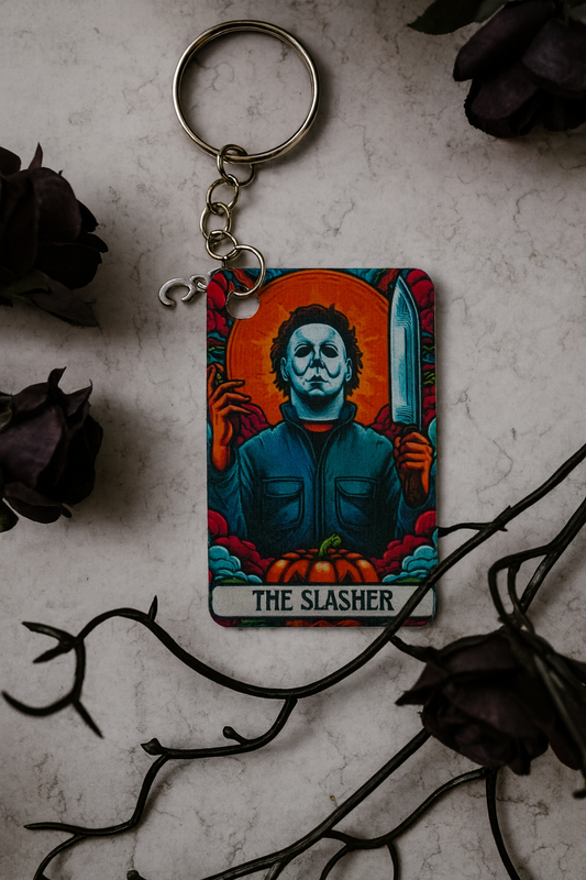 Keychain with 'The Slasher' design on a textured surface with dark roses and branches.