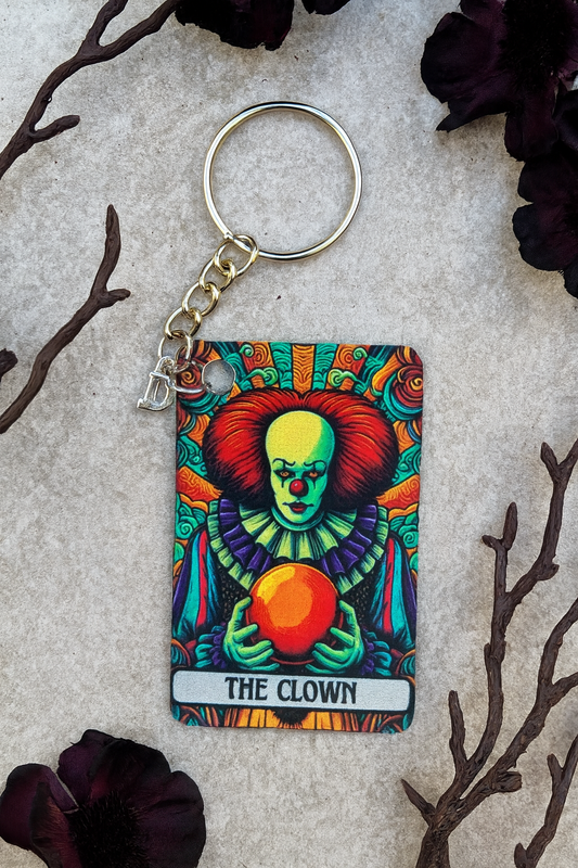Colorful keychain with 'The Clown' design on a textured surface with dark flowers and branches.